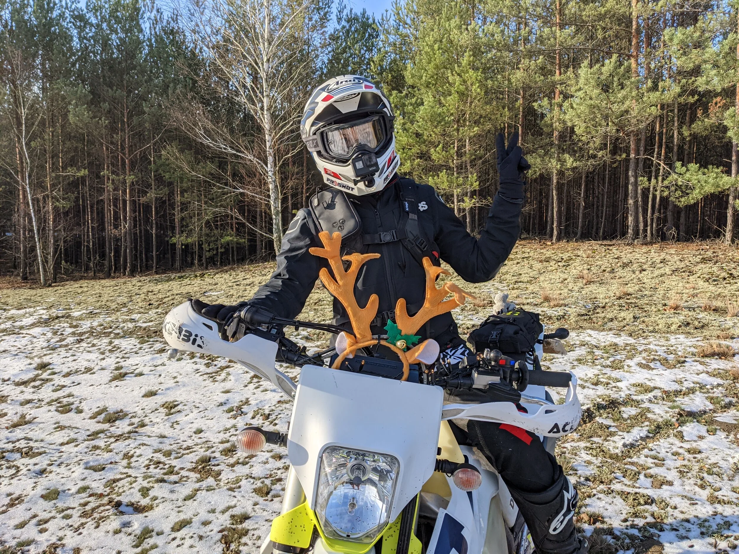 Motocyklista w kasku na Husqvarnie z reniferowymi rogami na ośnieżonej polanie